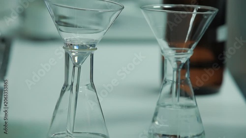 Close-up of pouring clear liquid into an Erlenmeyer flask through a glass funnel in a laboratory.