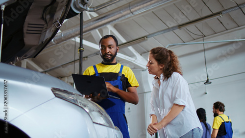 Fotografie Certified engineer in car service picks torque wrench from work station bench, using it to tighten bolts after replacing engine, african American garage worker fixing client automobile