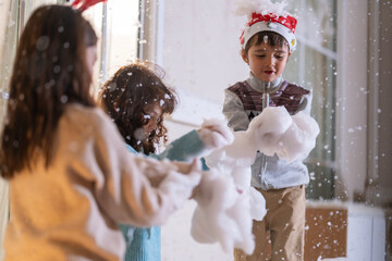 Children in Santa hats and reindeer antlers gather by a glowing decorated Christmas tree opening gifts at home.