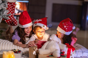 Happy children play with soft fake snow by a window during a festive Christmas morning celebration indoors at home together.