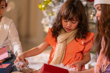 Smiling girl hugs a soft teddy bear gift beside the Christmas tree during a joyful family holiday celebration.