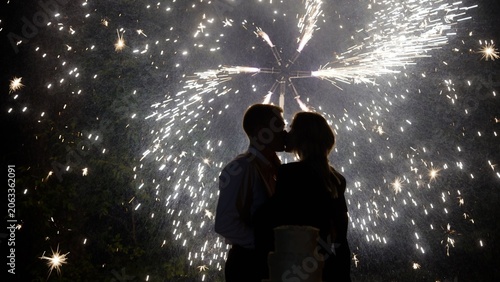 Silhouette of bride and groom kissing with fireworks and wedding cake