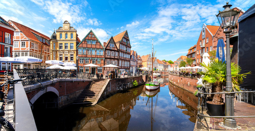 Foto Historic harbor of Stade with half timbered houses, restaurants, visitors and traditional sailing vessel beneath blue sky with reflections in the water