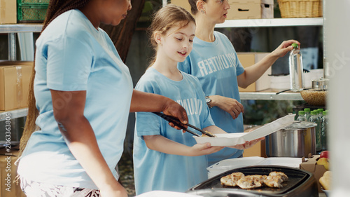 Принти на полотні Side-view of female volunteers giving the homeless and underprivileged free food, volunteers helping at a non-profit food drive by providing refreshments and assistance to less fortunate