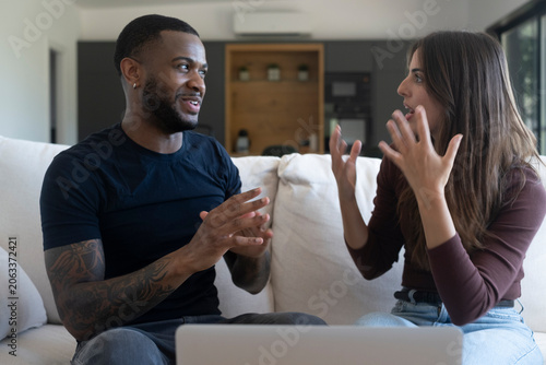 Photos Young couple having an intense discussion on a sofa at home, gesturing passionat