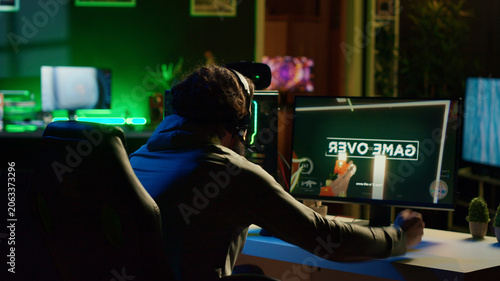 Bild auf Leinwand Angry man frustrated after losing science fiction FPS video game level in RGB lit apartment late at night, upset gamer raging, punching table after failing in online multiplayer shooter