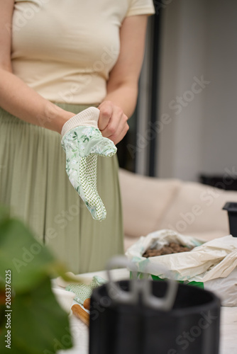 Person puts on gardening gloves for plant care near pots, tools and clay pebbles