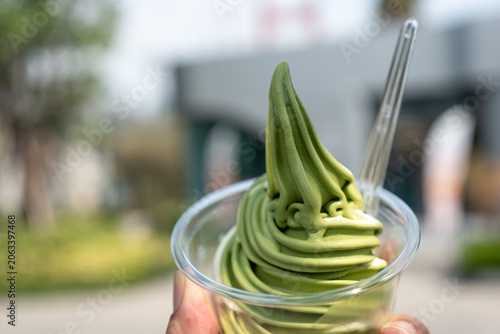 Hand holding a transparent cup of matcha green tea soft serve ice cream.