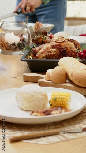 Vertical video: Picking up knife, host in green shirt slicing roast in pan at home serving family