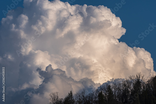 Towering illuminated cumulus cloud above a forested ridge against a deep blue sky at sunset in Warren County, Pennsylvania, USA