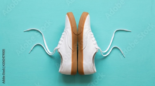 Pair of classic white canvas sneakers with gum rubber soles on a bright turquoise background. Flat lay, top view, minimalist fashion concept.