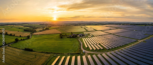 Aerial View of Expansive Solar Farm with Rows of Solar Panels under Vibrant Sunset in Rural Landscape