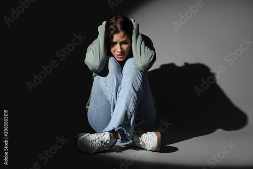 Scared young woman sitting on dark background