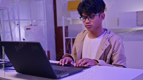 Focused Male IT Student Typing On Laptop Keyboard In Neon Workspace