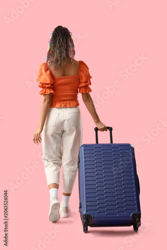 Young African-American woman going somewhere with her baggage on pink backgro...