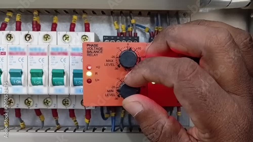 Technician hands adjusting the minimum level dial knob on a phase voltage balance relay inside industrial automation control panel
