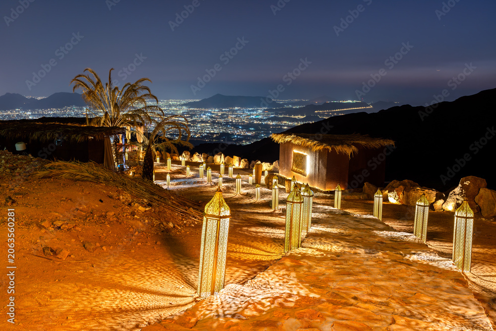 Fototapeta premium Traditional illuminated lanterns line a rocky path at Jabal Uhud viewpoint, offering a scenic night view of the city lights in Madinah, Saudi Arabia
