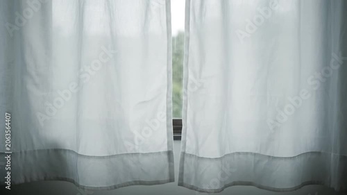 A pair of white sheer curtains gently blowing in the soft breeze by a window.