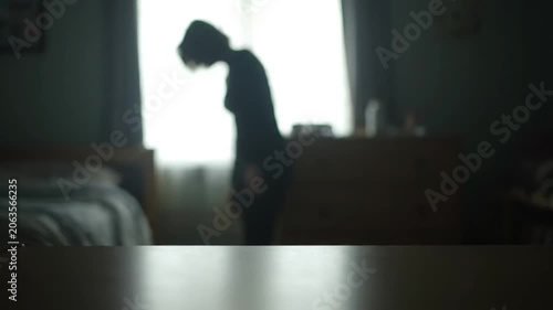 A silhouette of a lonely woman standing in a dimly lit bedroom.