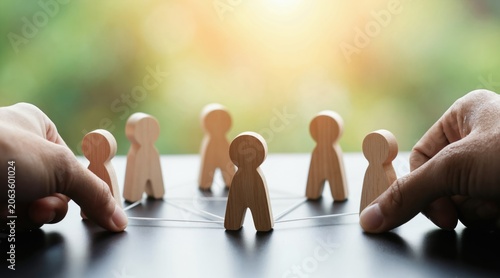 Small wood figures form network. Hands connect people icons with string. Teamwork and strategy develop organisation. Business concept connection, collaboration builds success.