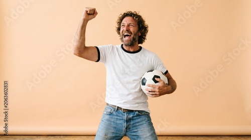 Excited man cheering while holding a soccer ball with t shirt football cheering celebration background enthusiasm competition lifestyle