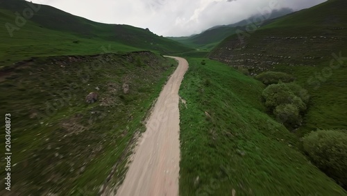 Dirt path through green hills under cloudy sky