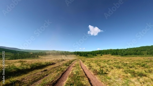 Dirt road through open field under blue sky and cloud