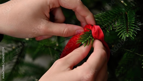 Hands decorating christmas tree with red ribbon and green branches