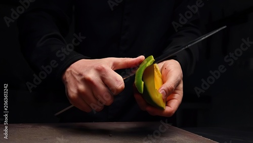 Hands cutting colorful bell peppers with a knife in dark setting