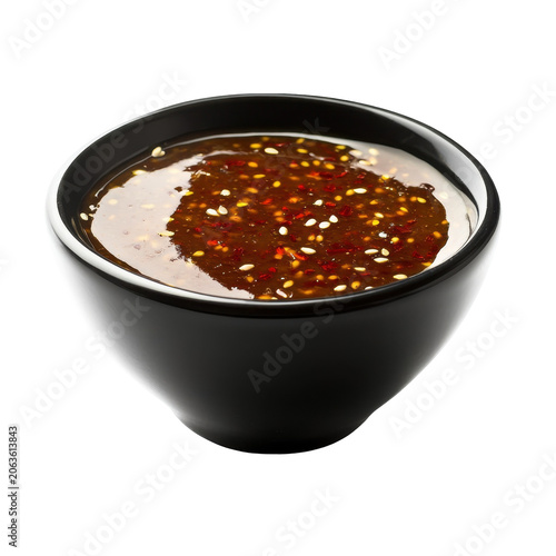 Glossy dark sauce with sesame seeds and chili flakes in a black bowl isolated on white background