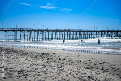 Children and adults play at Oceanside City Beach with pier and surf on sunny day in California