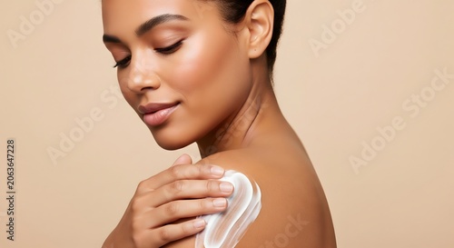 Beautiful young woman applying moisturizing body lotion on her shoulder