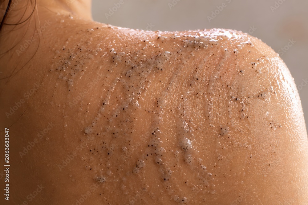 Fototapeta premium Woman applying exfoliating body scrub on shoulder skin. Skin care and beauty treatment at home. Cosmetics procedure for natural body peeling, smooth hydration and rejuvenation process.
