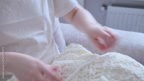 Female hands knitting a cozy white blanket using super chunky plush yarn at home.