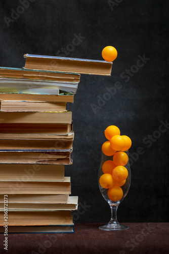 Still life with a stack of books and orange balls in a glass.