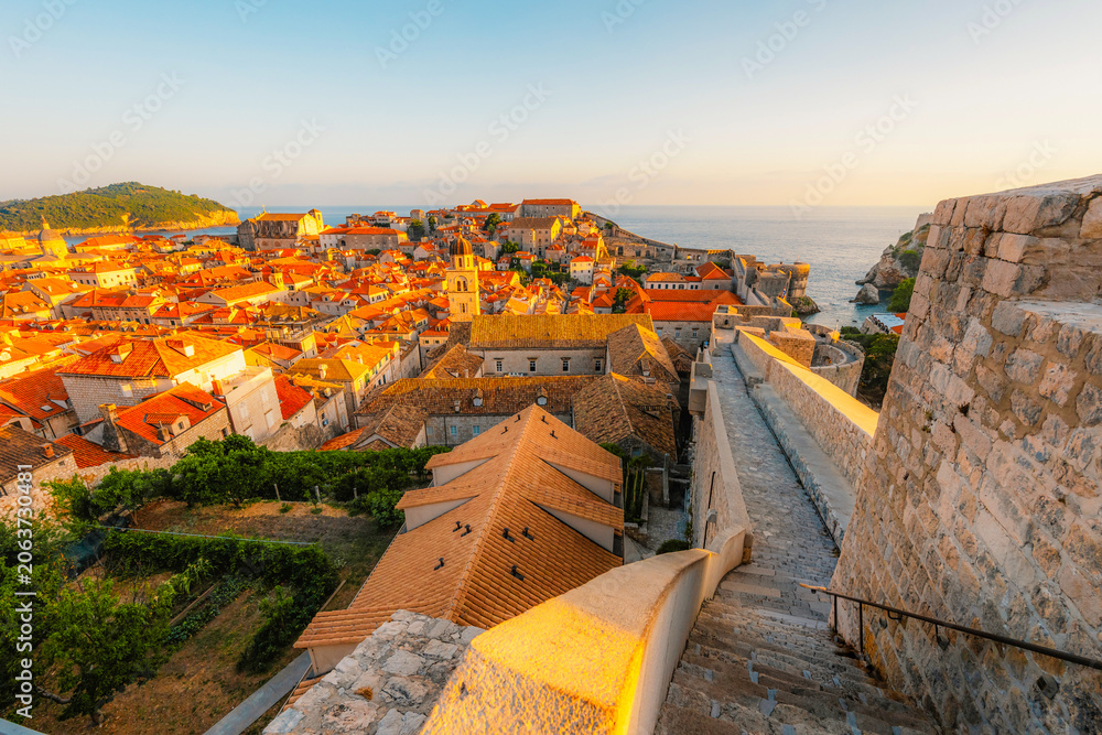 Obraz premium Golden hour panorama of Dubrovnik's historic fortifications and old port at dusk, sunlight on ancient stone walls and Mediterranean architecture in Croatia