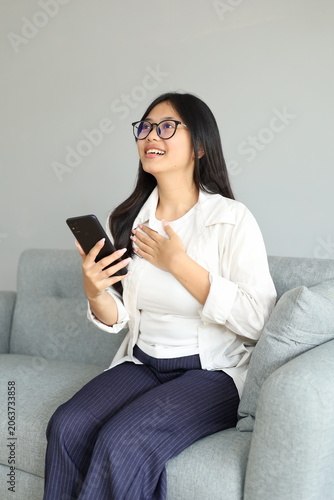 A happy young woman, feeling relieved or fortunate, holds her chest and looks up, celebrating a victory or receiving a message containing good news.