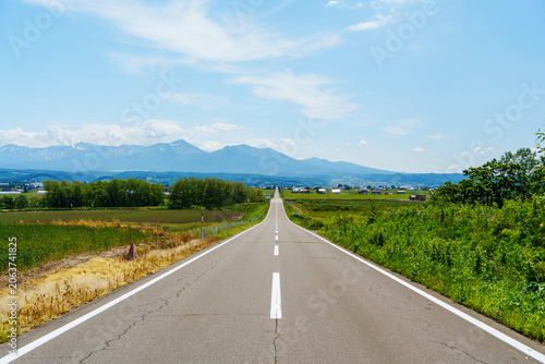 Foto A stunning perspective shot of a long straight paved road leading directly toward the magnificent Daisetsuzan mountain range in Furano, Hokkaido