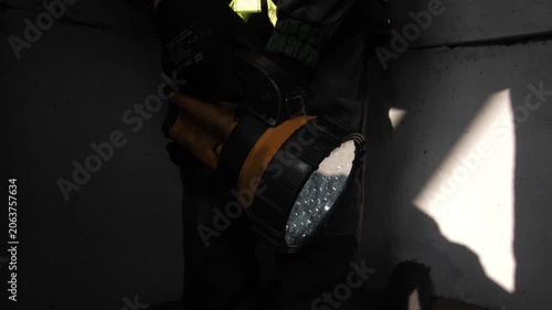 Man worker in uniform shining lit flashlight on construction site at work.