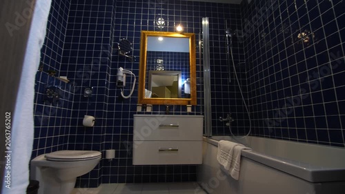 Modern bathroom with blue tile, toilet, bath, bidet, sink and wooden mirror.