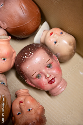 Collection of vintage doll heads scattered in a cardboard box, some with chipped paint