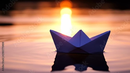 A delicate paper boat sails gently on the water's surface, reflecting the warm glow of the setting sun, evoking a sense of peace and wonder