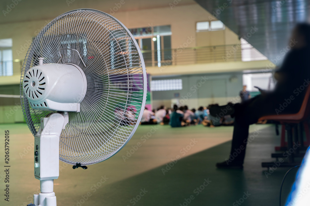 Naklejka premium White Pedestal Fan in Indoor Hall with Blurred People Background