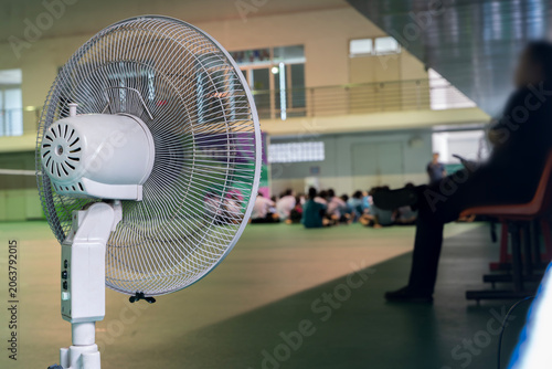 White Pedestal Fan in Indoor Hall with Blurred People Background