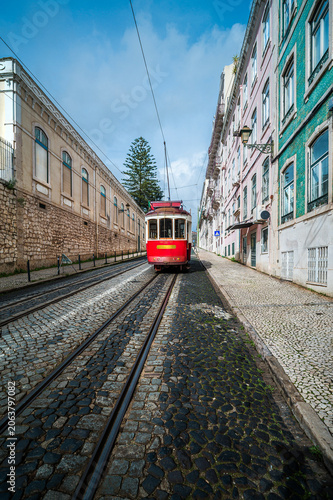 Historic red funicular tram traveling up the steep. Traditional cobblestone street in Lisbon. With classic Portuguese architecture lining the sides under a blue sky