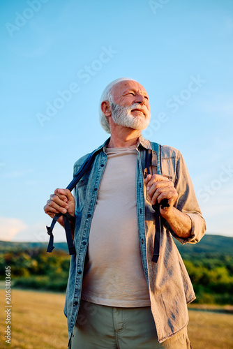 Foto Happy senior man smiling while holding backpack straps, enjoying outdoor adventu