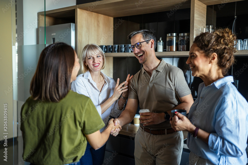 Naklejka premium Diverse colleagues shaking hands and laughing in office kitchen