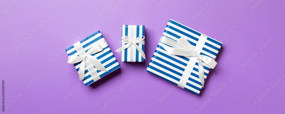 Fototapeta premium wrapped Christmas or other holiday handmade present in paper with White ribbon on purple background. Present box, decoration of gift on colored table, top view