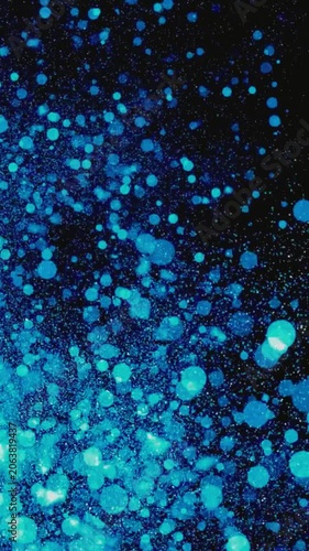 Abstract glowing blue bokeh particles floating and shimmering against a dark background. Magical sparkling light dust vertical video