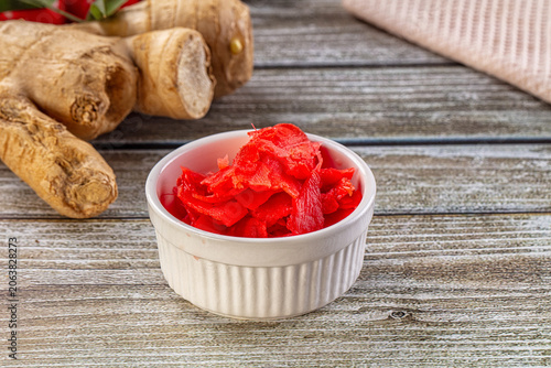 Fotografie Red pickled ginger in white bowl with fresh horseradish roots on wooden table
